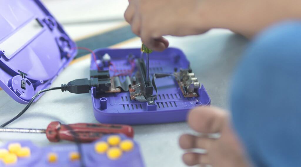 Close up of child's hands as they repair video game parts with screw driver.