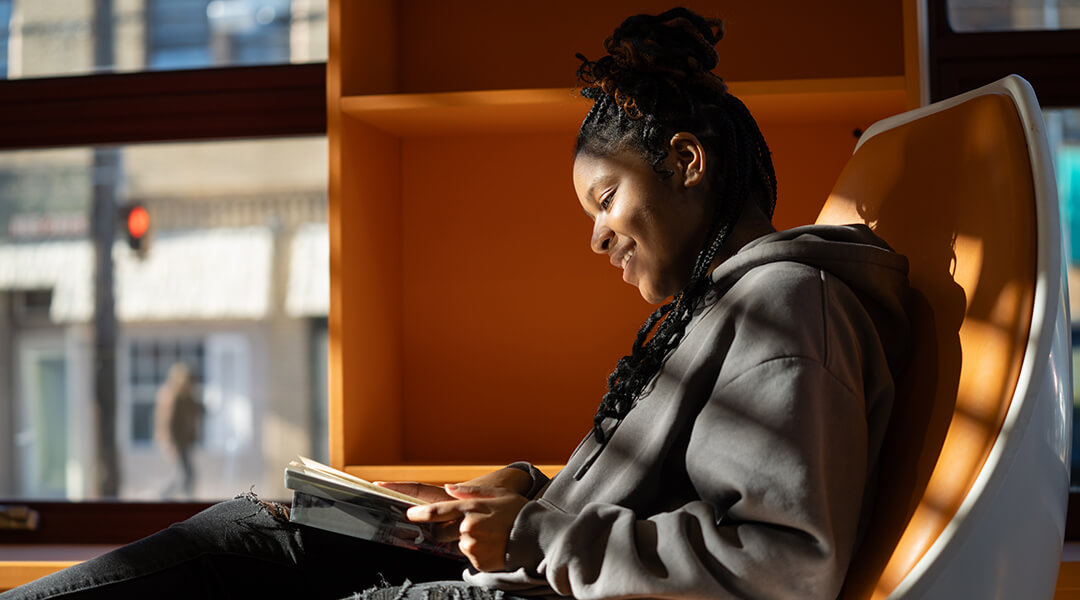 A smiling teen reads in the TeenSpace.