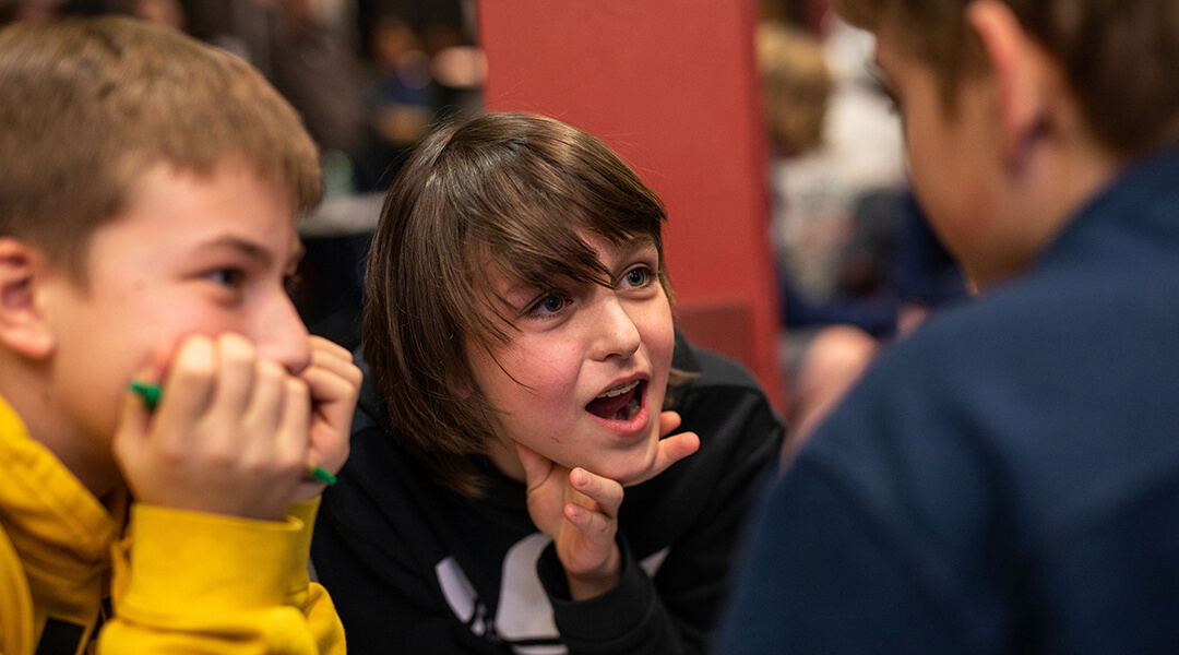 Three tweens huddle close together during a trivia game at the Library.