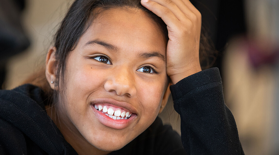 Close-up of a teenager smiling, propping their head up with one hand.