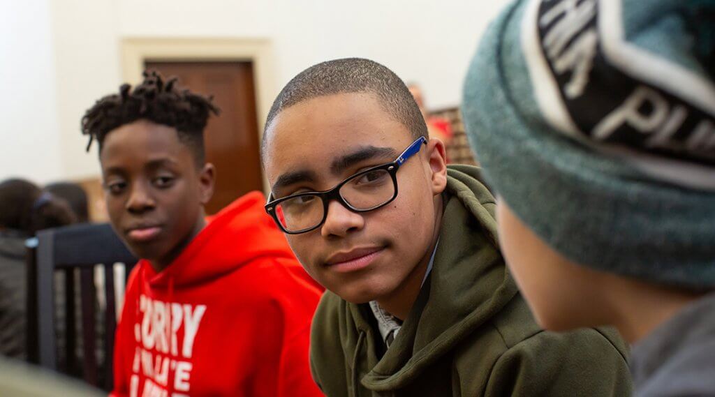 Close-up of three teenage boys, around 13, sit together in the library.