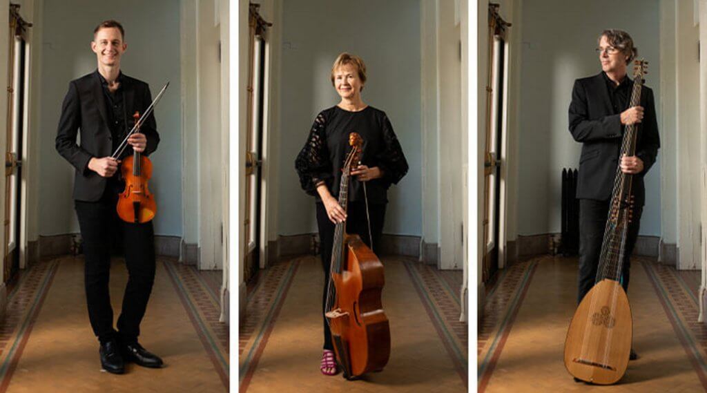 Three musicians wearing black pose with their string instruments in a hallway.