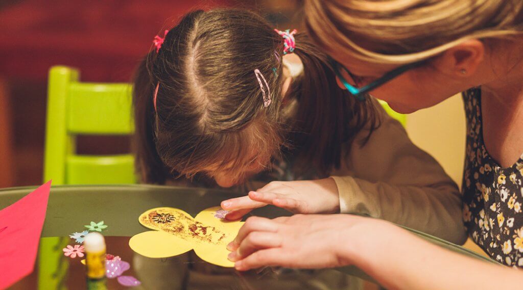 A child and caregiver lean over a craft together.