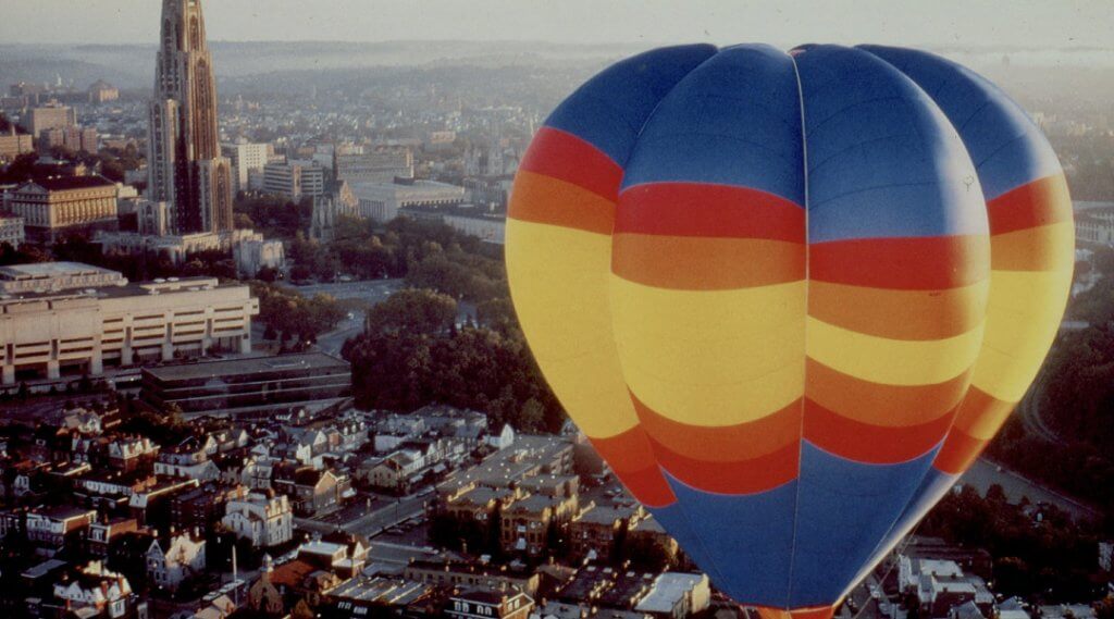 Yellow, red and blue hot air balloon flying over Oakland and the Cathedral of Learning