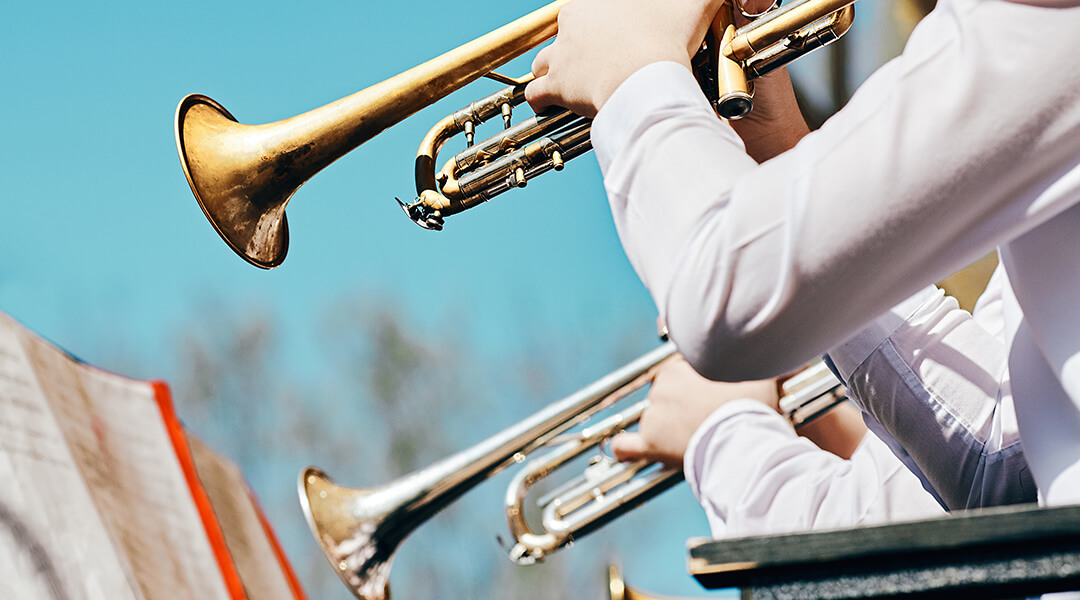 A closeup of several trumpeters playing in a brass band in the summer in a city park.