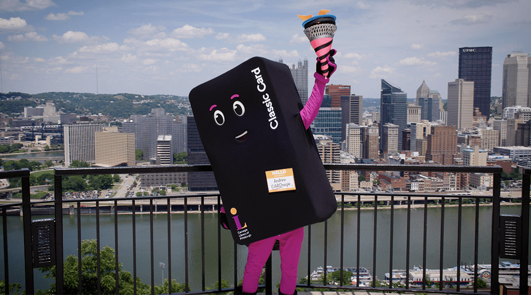 Library card mascot with Summer Reading torch on Mt. Washington with Pittsburgh skyline in the background