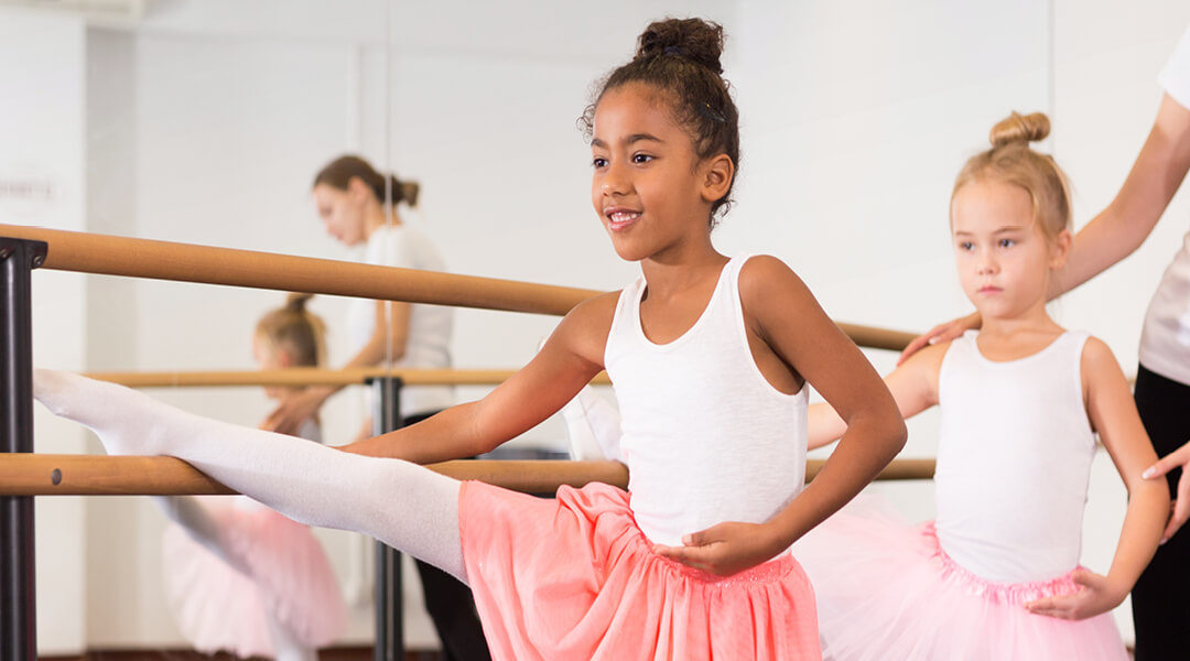 Two children, about seven, are gently corrected at a barre during ballet practice.