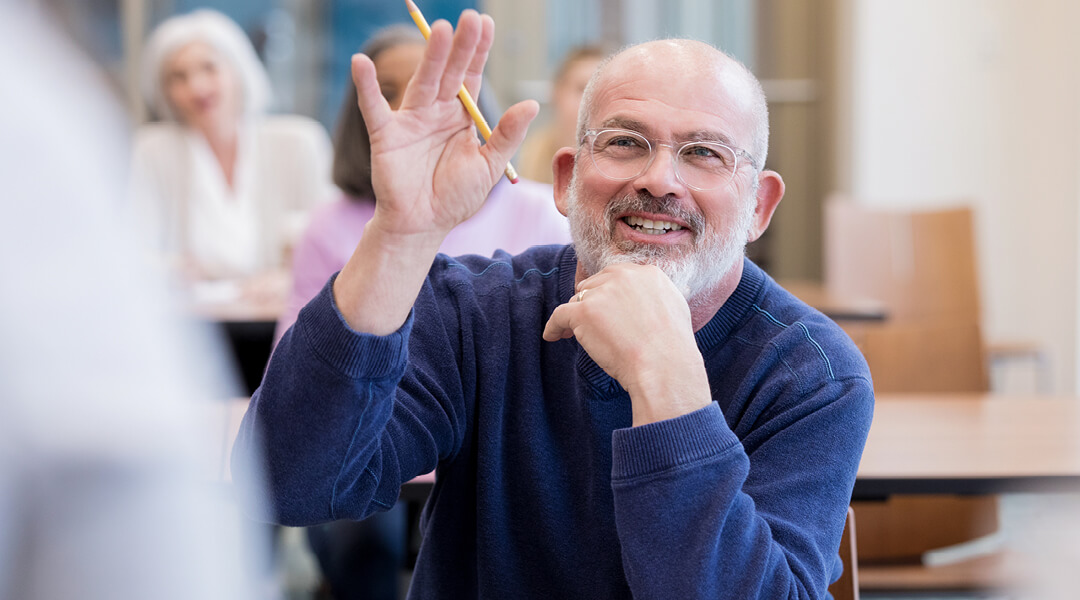 A middle-aged adult raises their hand during a workshop presentation.