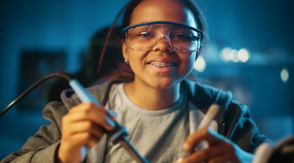 A smiling teen with braces and safety glasses uses tools for a STEM project.