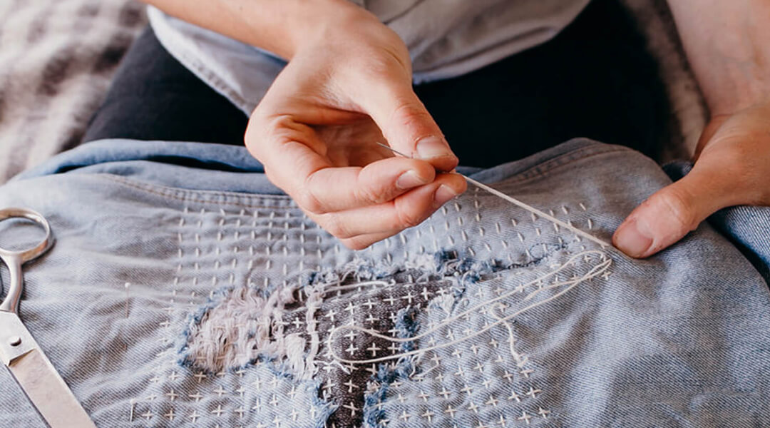 Close-up of a needle pulling thread through a denim shirt that's being patched.