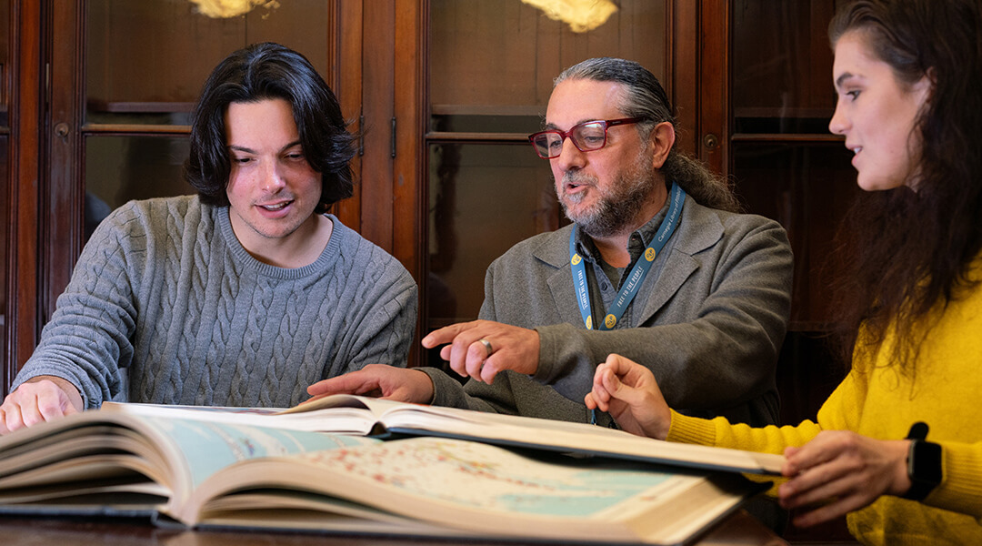 A librarian shares an oversized book from an archive collection with two patrons.