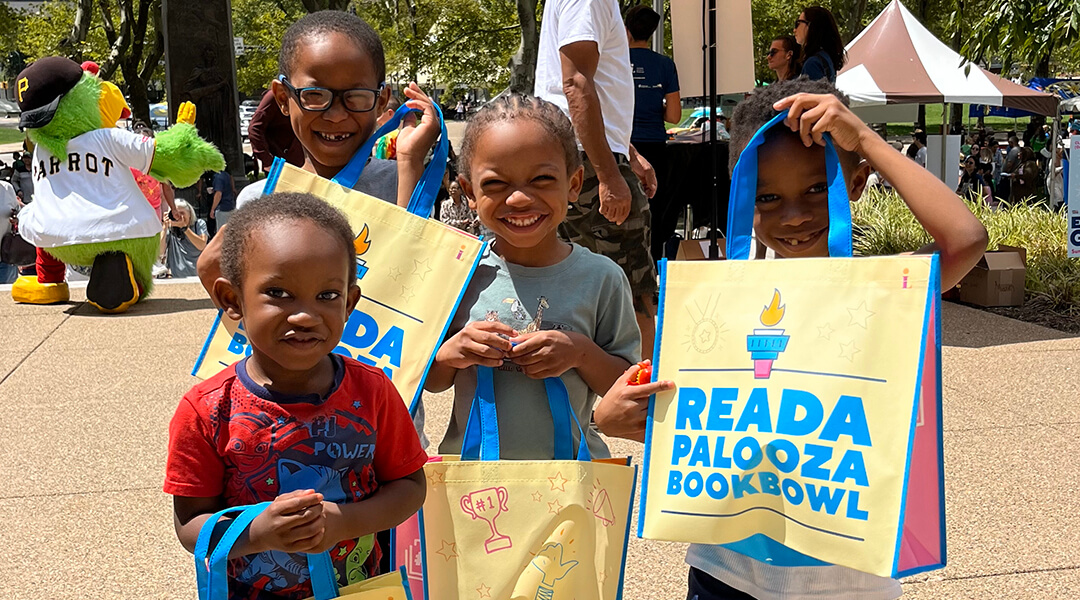 Four smiling kids holding Summer Reading 2024 bags at Extravaganza