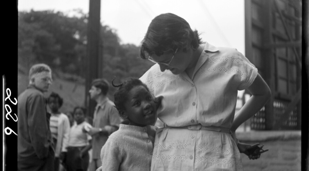 Scan of an historic photo featuring a woman posed with her arm around a young child outside.