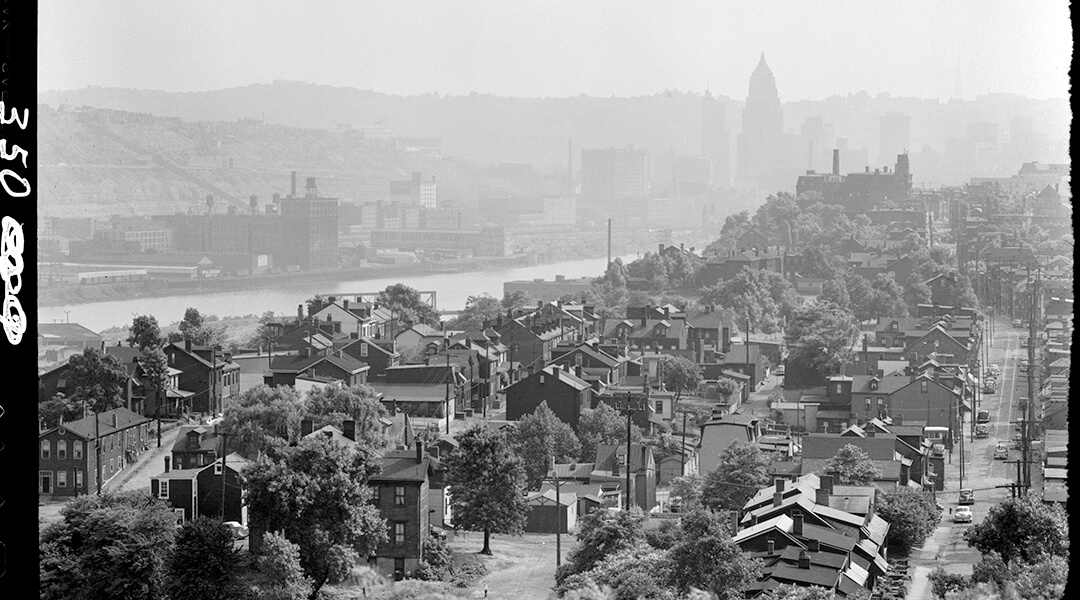 Scan of an historic picture of a Pittsburgh with a view across a river and the forming shapes of downtown buildings in the distant background.