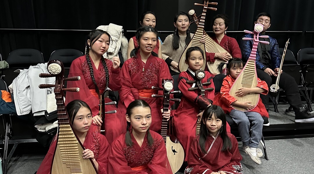 Group of 10 people, mostly young women, in similar gowns holding musical instruments