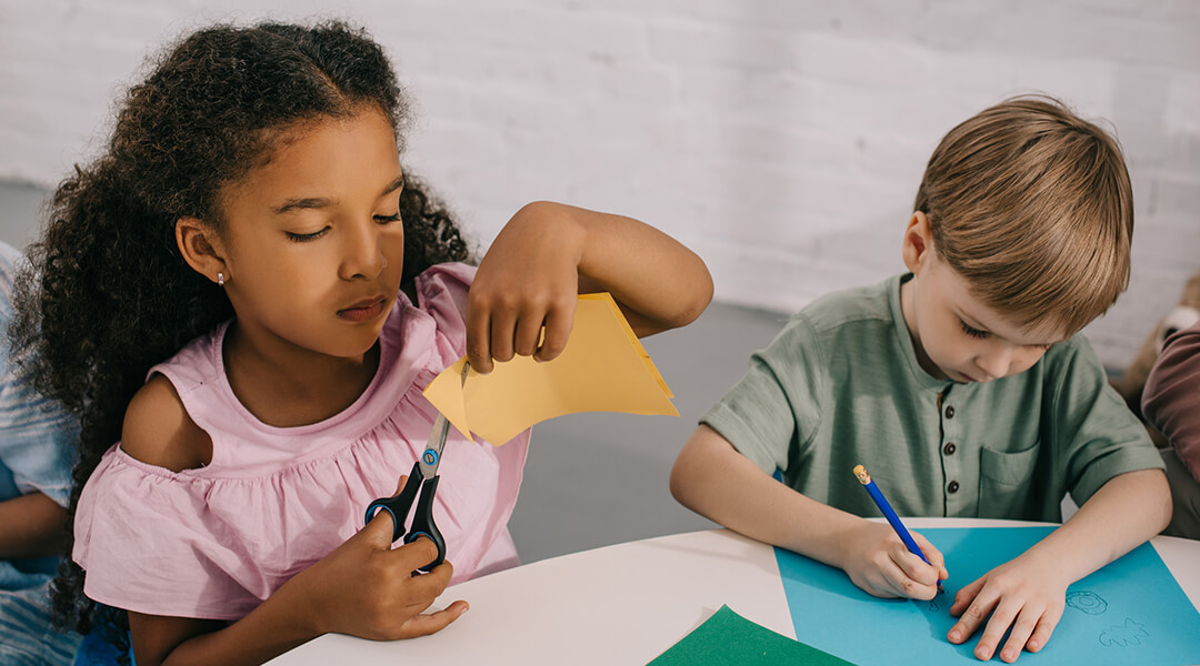 Two elementary school-aged children work on paper crafts in class.