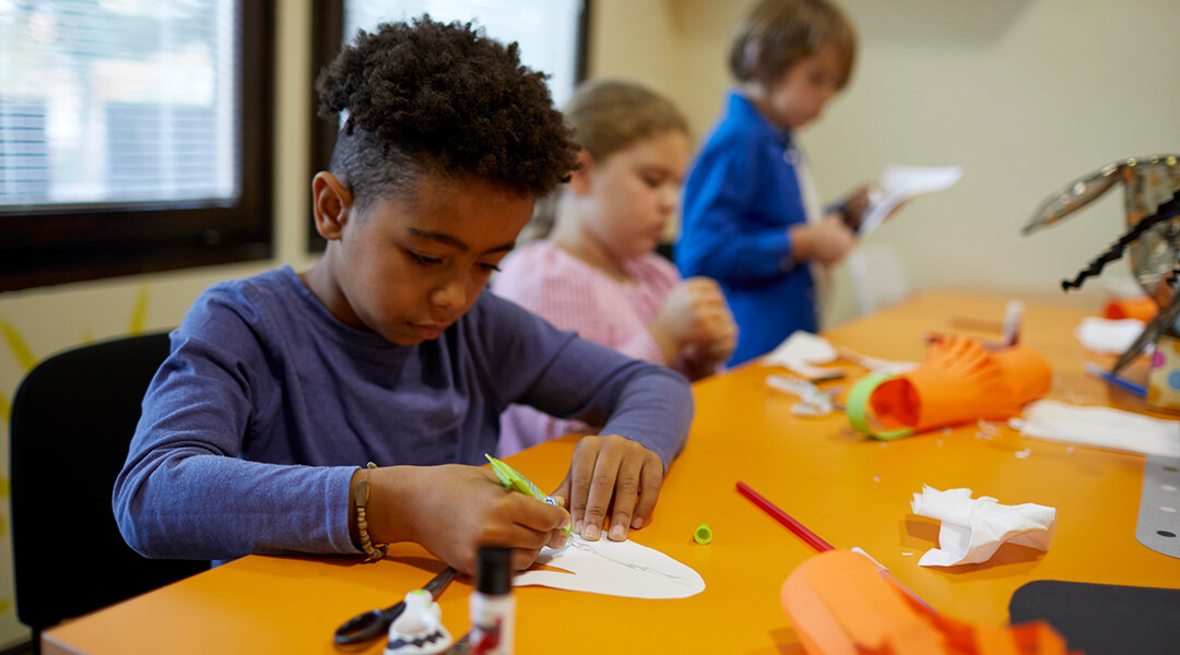 Three elementary aged children work on craft projects during class.