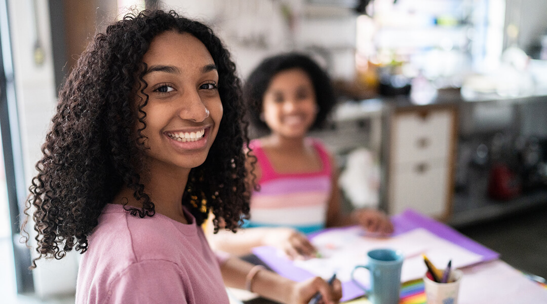 Portrait of happy teenager girl drawing or studying with sister at home