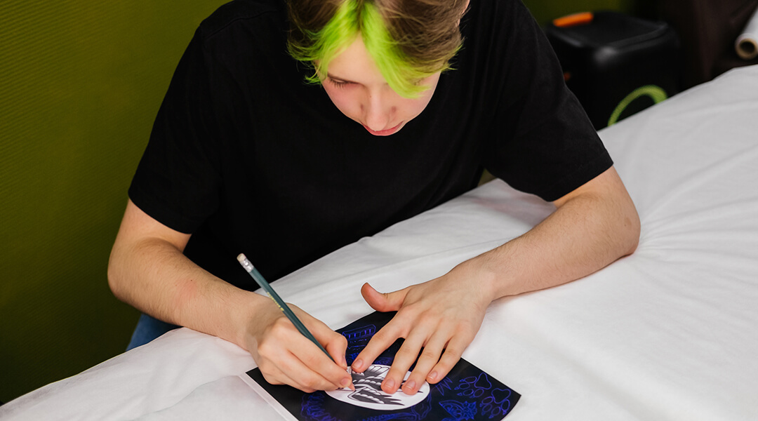 A teenager with colored hair draws sketches indoor.