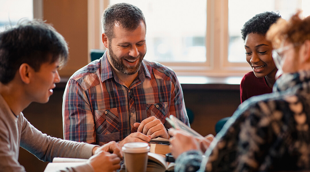 Small group of people with a mixed age range sitting at a table, discussing and reading books together.