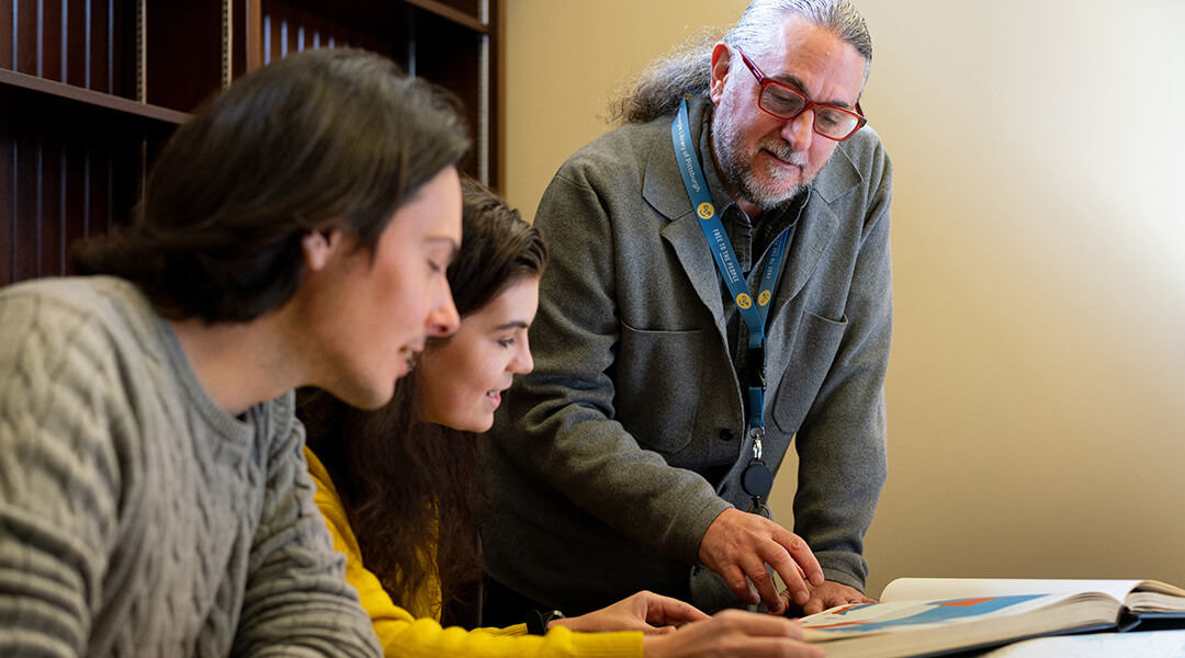 A librarian reviews an oversized map book with two patrons.