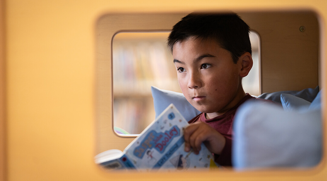 A child, about seven, reads in a cubby in the library.