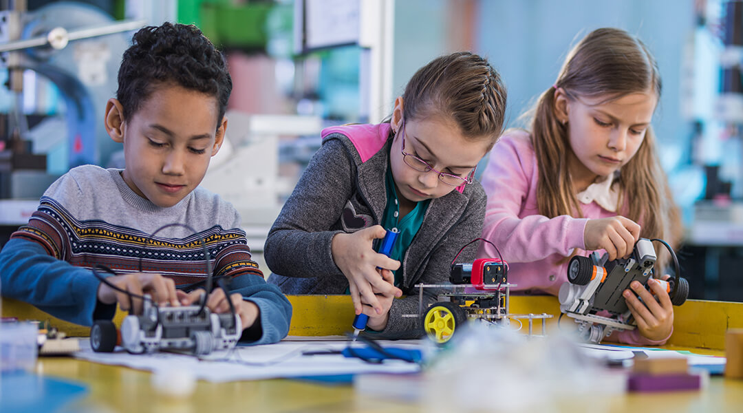 Three elementary school students working on small robotic projects in science lab.