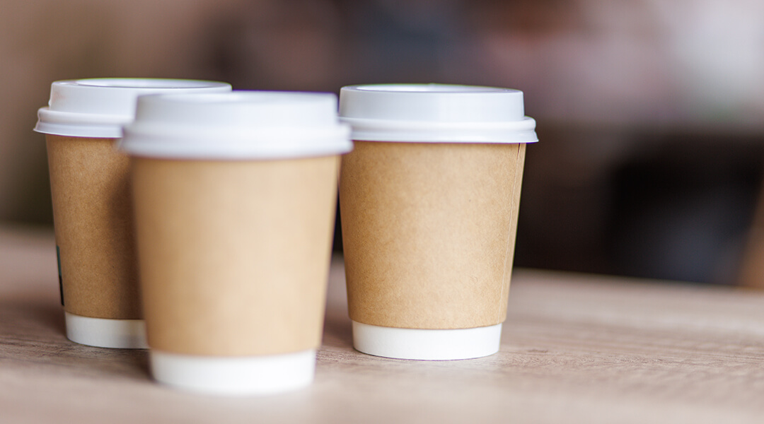 Close up shot of three cups of takeaway coffee on a desk.