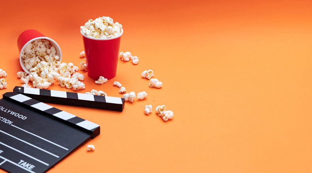 Popcorn in red cups and movie clapper board on an orange background.