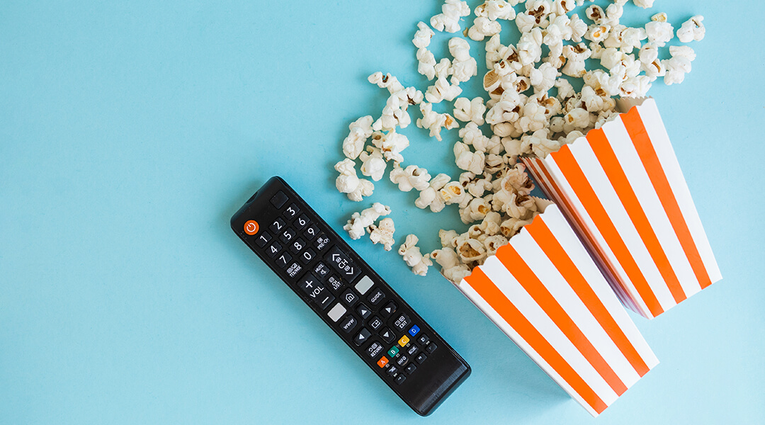 Popcorn and TV remote on a blue background.