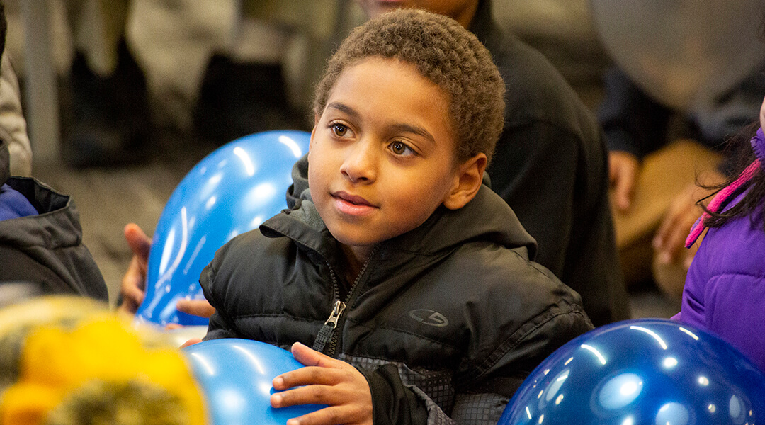 A child, about three, holds a balloon while watching a storytime presentation.