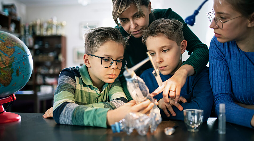 Teacher instructing three children, ages 8-14, demonstrating how carbon dioxide increases temperature in a plastic bottle.