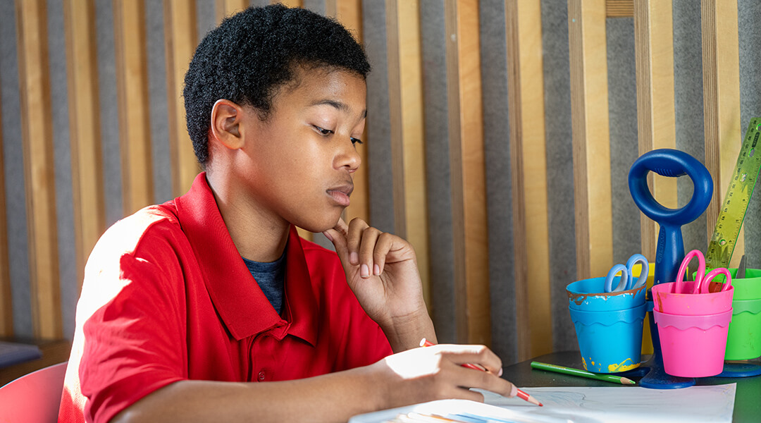 A young teenager colors with colored pencils.