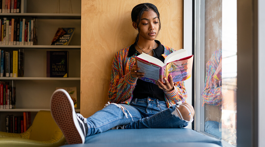 A teenager reads in a window seat in the library.