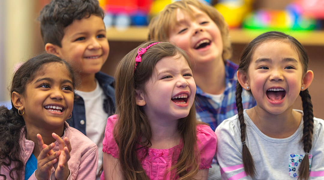 Five pre-school age children laugh during a storytime reading.