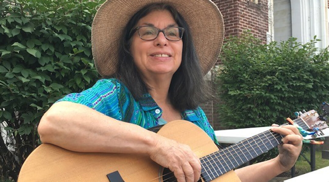 Performer Granny Sue playing an acoustic guitar at a picnic table.