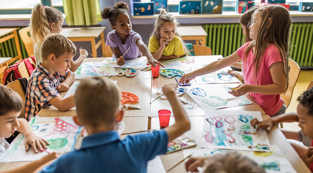 A diverse group of kindergarten aged children paint together in a classroom.